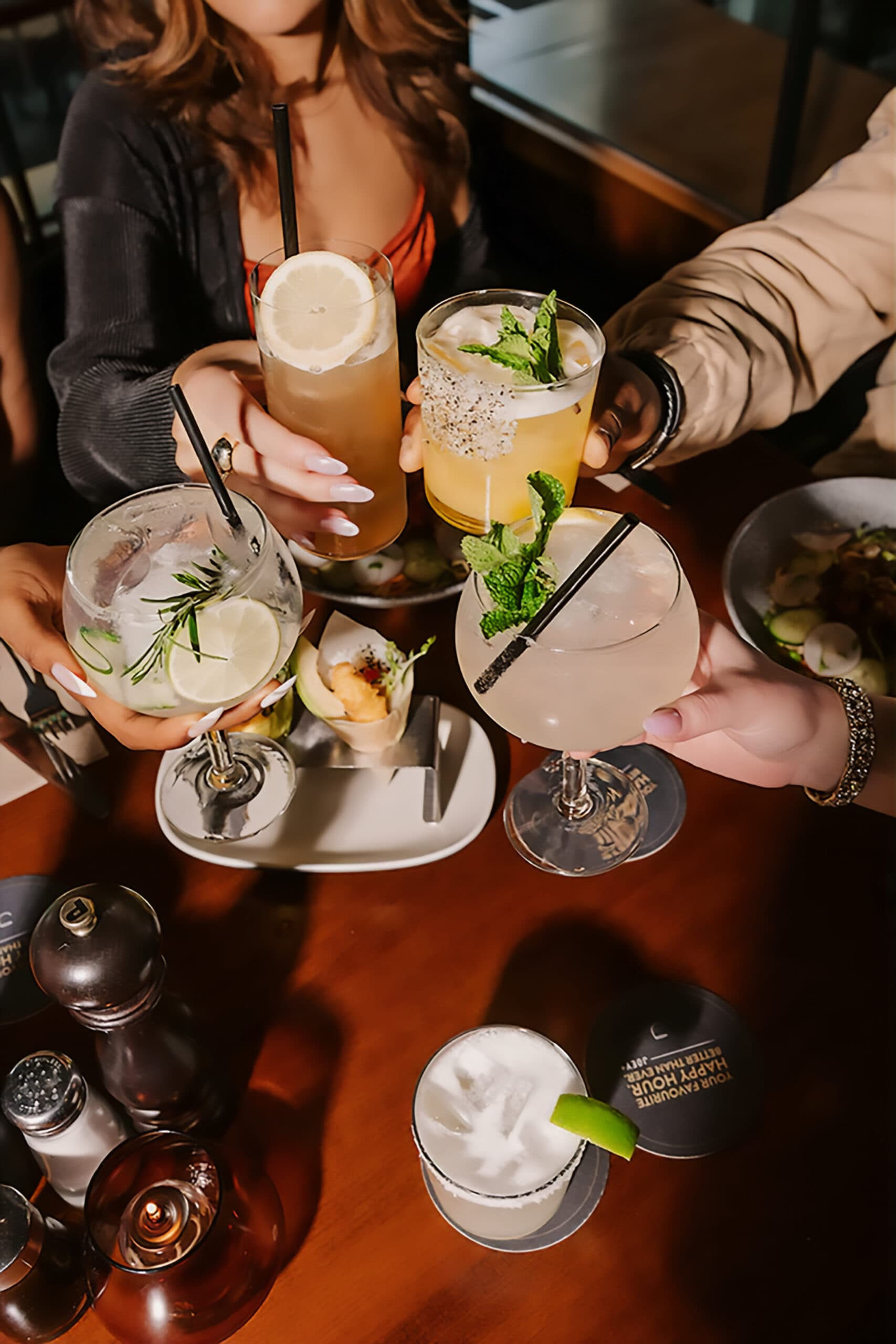 Several people clinking cocktails together over a wooden table.
