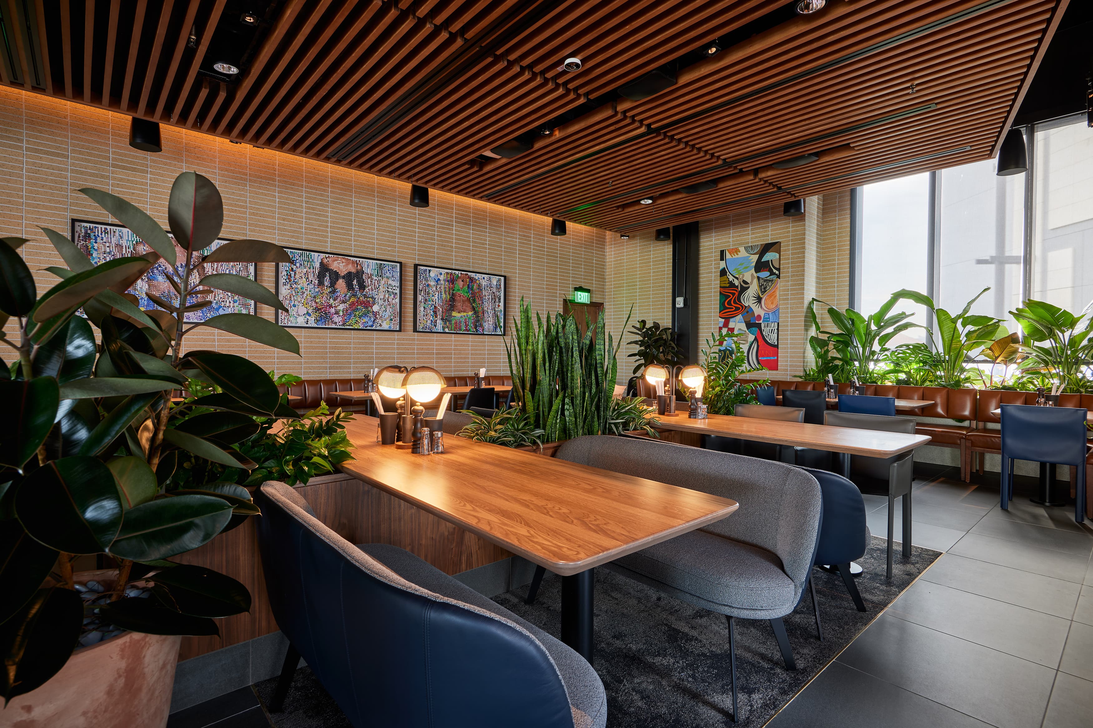 Restaurant interior with wooden tables, plant accents, modern art decor and natural light.