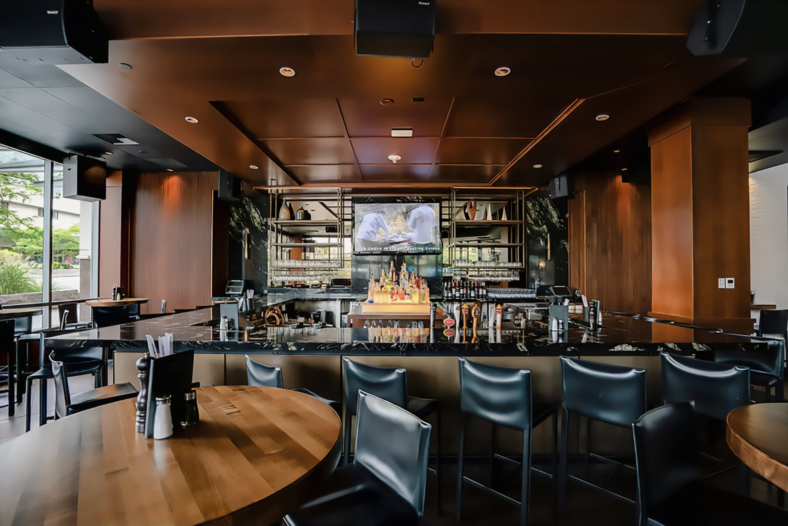 Sleek high-top bar with black stools, natural lighting from floor-to-ceiling windows and a flat-screen TV.