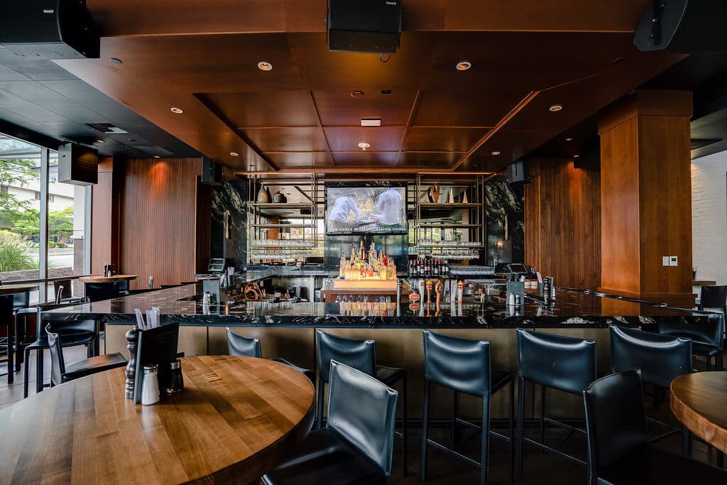 Sleek high-top bar with black stools, natural lighting from floor-to-ceiling windows and a flat-screen TV.